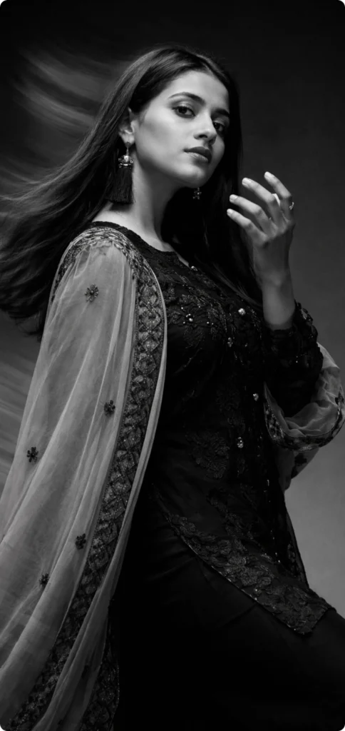 A female model in a traditional black and grey embroidered outfit poses for a portrait inside a professional studio.